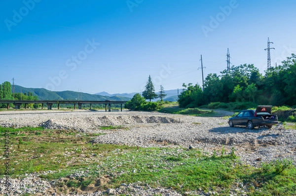 Obraz Road trip on car. A car standing near the river on a pebble rocks in the mountains. Wild nature background