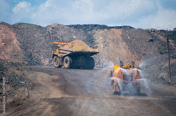 Fototapeta Heavy truck pours the road with water in the iron ore quarry. Dust removal, protection of the environment. Irrigation of the road from dust	