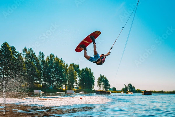 Obraz Młody człowiek wakeboarding na jeziorze, robiąc Raley, frontroll i skakał z kickerów i suwaków. Wakeboard.