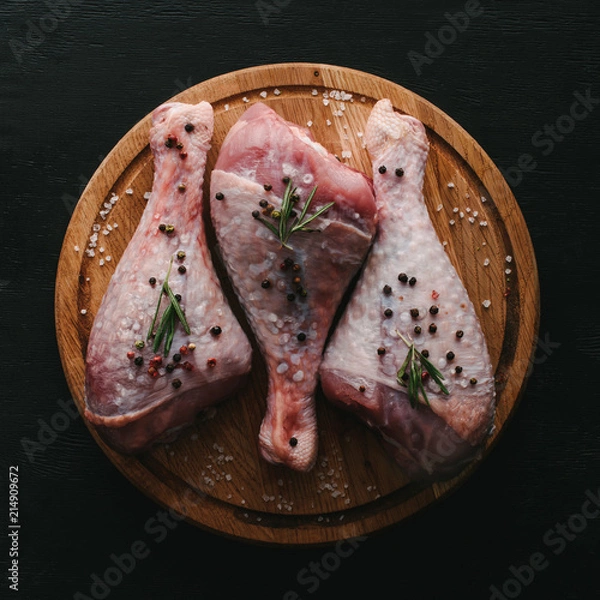 Fototapeta top view of raw turkey legs with pepper corns and rosemary on wooden cutting board