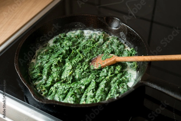 Obraz Preparation of a dish - baby spinach boiled in garlic sauce in a cast-iron pan.