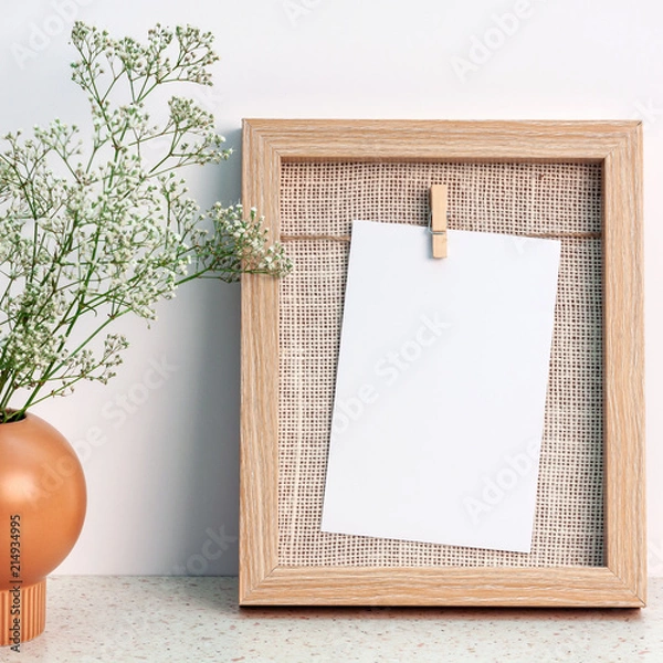 Fototapeta A wooden natural frame and an orange vase with an original shape with white flowers against a white wall
