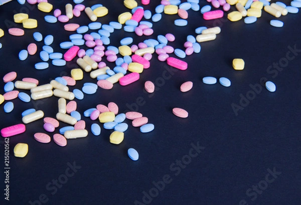 Obraz Variety of colorful pink and blue spilled pills on a black background with text space. Healthcare expenses, savings, insurance concept. Mixing pills, addiction, doping, excess, disease.