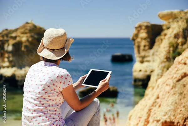 Fototapeta Back side view of person sitting holding tablet computer on ocean sunny natural background. Traveler having fun on international travelling lifestyle, technology social communication, amazing nature.