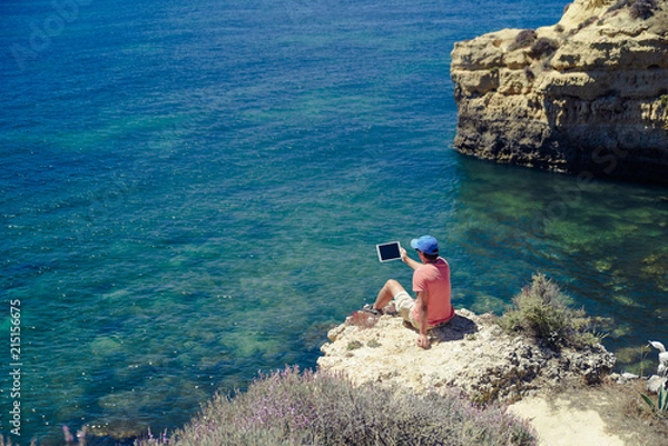 Fototapeta Back side view of person sitting holding tablet computer on ocean sunny natural background. Traveler having fun on international travelling lifestyle, technology social communication, amazing nature.