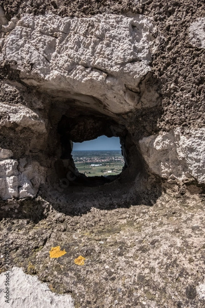Fototapeta Square hole in an ancient stone wall with landscape view on the background. No people.