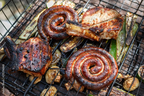 Obraz Twisted sausages, pork steak, mushrooms and zucchini cooked on grill.