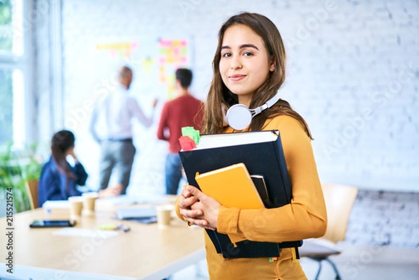 Obraz Kobieta studentów stojących w klasie trzymając książki. Portret młodej kobiety, patrząc na kamery w pomieszczeniu