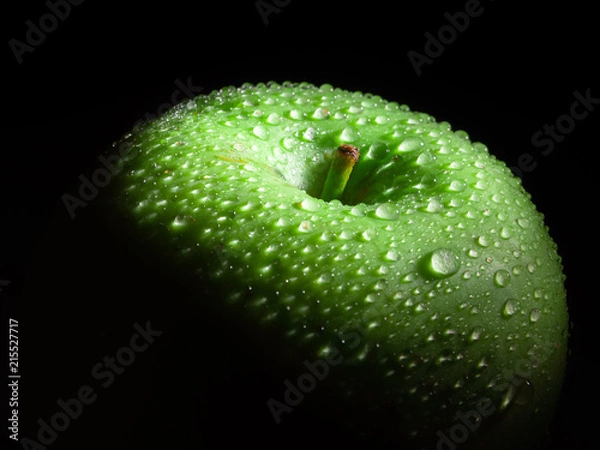 Fototapeta Green ripe apple with water droplets on a dark background.