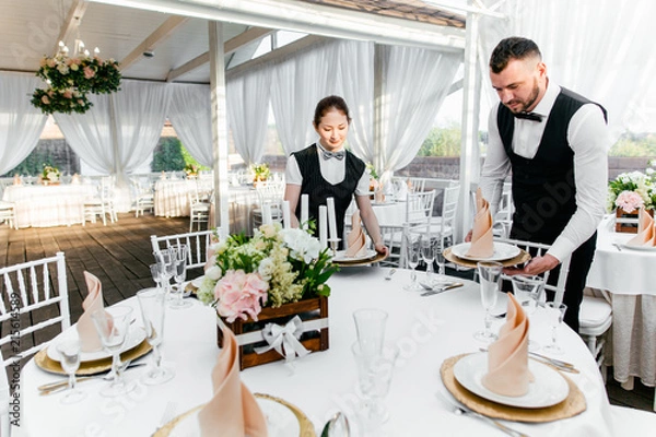 Fototapeta Two male and female waiters serve tableware on the table in the restaurant