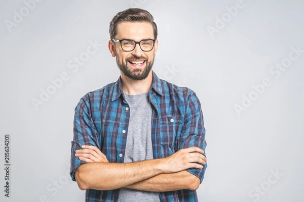 Fototapeta Happy young man. Portrait of handsome young man in casual shirt keeping arms crossed and smiling while standing against grey background