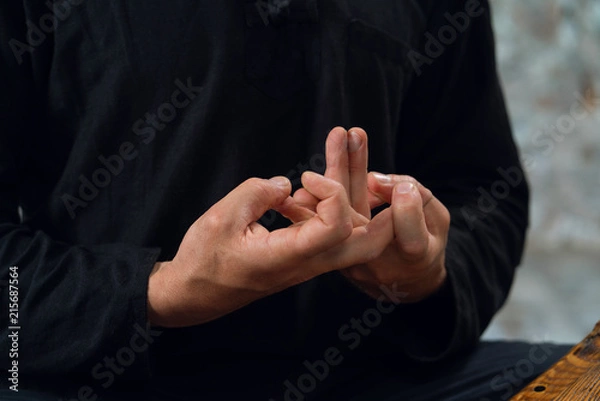 Obraz a man in black interlaced his fingers in mudra