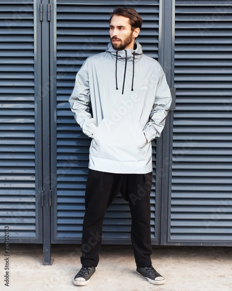 Fototapeta Modern materials in the fashion industry. Windbreaker from the rain. A bearded hipster man is posing in a fashionable silvery waterproof jacket made of new technological materials. Sneakers.