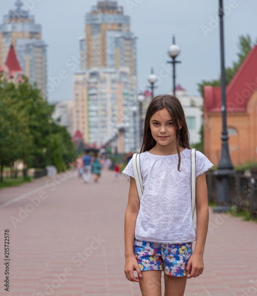 Fototapeta background. beautiful girl walks on the waterfront on a background of tall houses and green trees