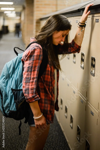 Obraz Sad high school student leaning against locker with backpack
