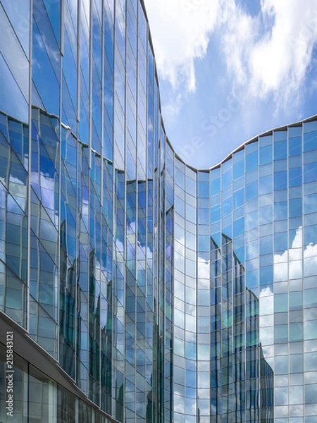 Obraz Modern glass building with reflection of blue sky and clouds.