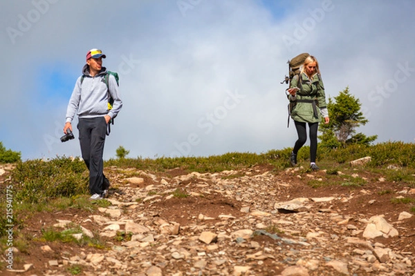 Obraz Travel Lifestyle and survival concept rear view. Hiking women  and men with backpack  enjoying the trekking, go to the mountains,  in the background a green field, mountains. 