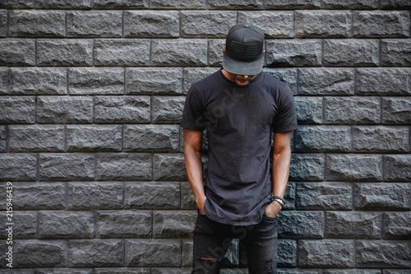 Fototapeta Handsome african american man in blank black t-shirt standing against brick wall