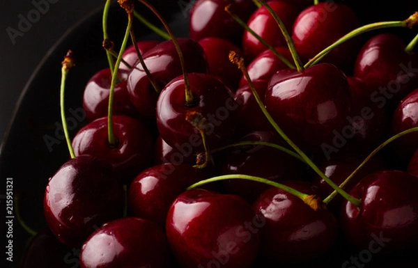 Fototapeta Bowl of cherries on a black background. Dark image of red cherries on a black reflective surface.