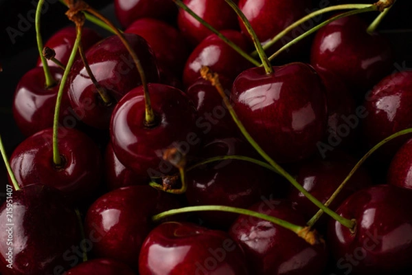 Fototapeta Bowl of cherries on a black background. Dark image of red cherries on a black reflective surface.