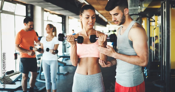 Fototapeta Two attractive women exercising with personal trainers