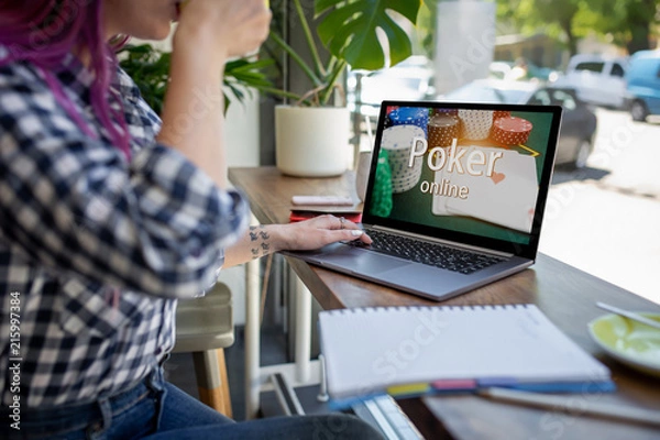 Fototapeta Side view of a young pink hair woman keyboarding on laptop computer with poker online on a screen while sitting in cafe.