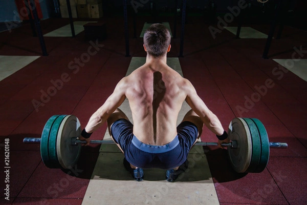 Fototapeta Muscular fitness man preparing to deadlift a barbell over his head in modern fitness center.Functional training.Snatch exercise.