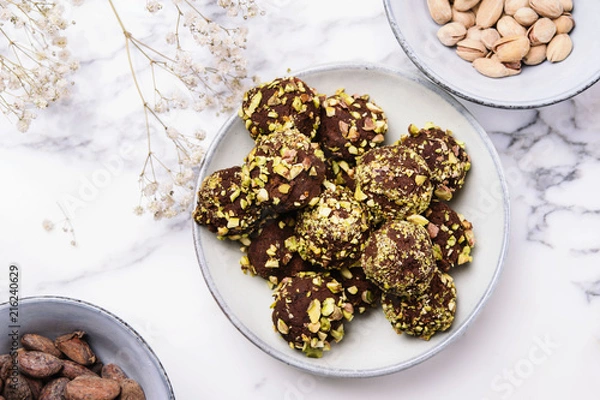 Fototapeta Homemade healthy vegan chocolate avocado truffles with pistachio in the bowl and ingredients on grey marble table. Organic energy vegetarian sweet balls