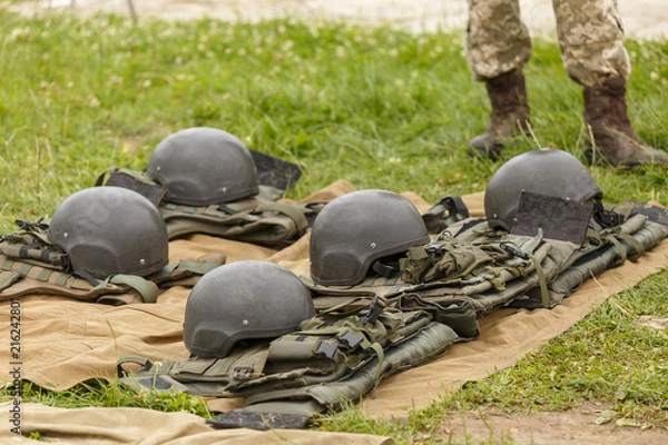 Fototapeta Camouflage combat flak jackets and helmets lined up on the ground