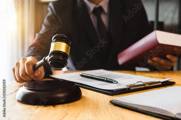 Fototapeta justice and law concept.Male judge in a courtroom  the gavel, working with digital tablet computer on wood table in morning light 