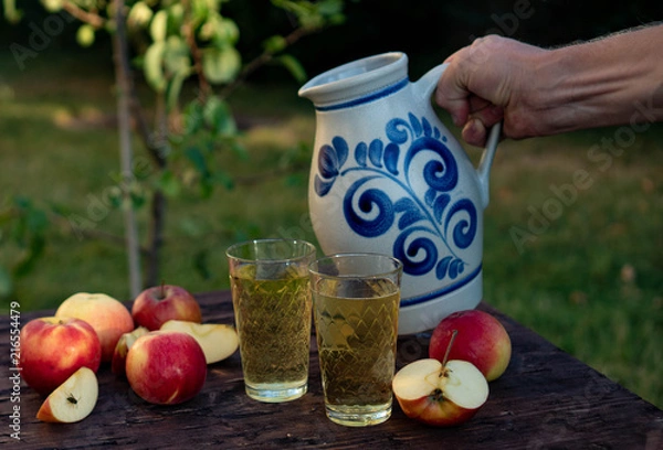 Obraz a man's hand pours Traditional apple wine in a refilled glass in the city of Frankfurt. A jug of wine on an old wooden table in the garden, around it apples