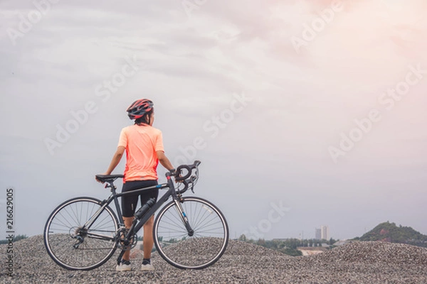 Fototapeta Young slim lady standing on top of a mountain with bicycle and enjoying valley view