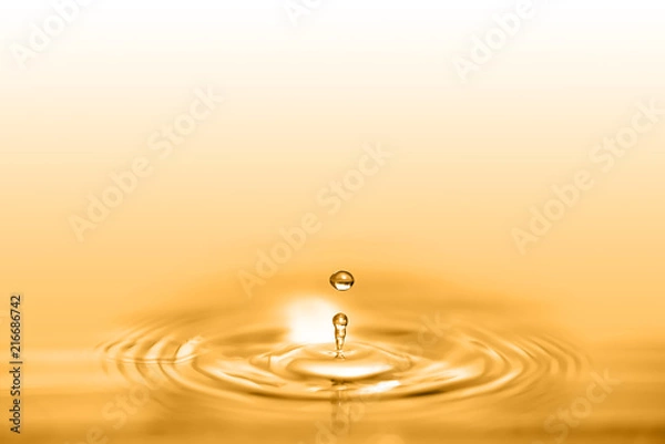 Fototapeta Closeup on drop of cosmetic golden oil liquid creating a circular wave.