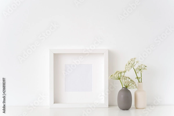 Fototapeta Interior white square frame mock up with a episcopal weed in vases near white wall. Mockup for quote, promotion, headline, design. Template for small businesses, lifestyle bloggers, social media