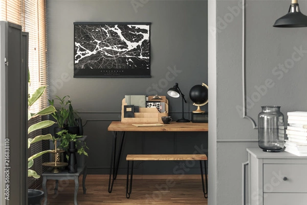 Fototapeta Map poster hanging on the wall in real photo of open space room interior with hairpin bench and desk with lamp, black globe wooden organizer and tea cup