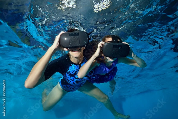 Obraz Happy family, mom and baby play in virtual reality helmets underwater in the pool. Close up. Shooting underwater. The horizontal orientation of the image
