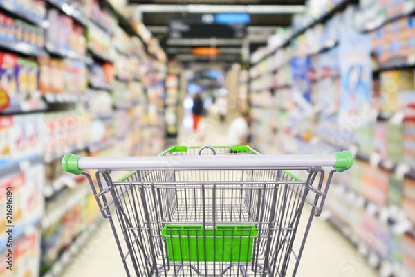 Fototapeta supermarket shelves aisle with empty shopping cart defocused interior blur bokeh light background