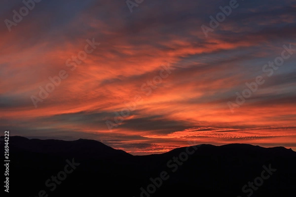 Fototapeta Reddish sunrise with clouds and mountains. Atmospheric effects concept