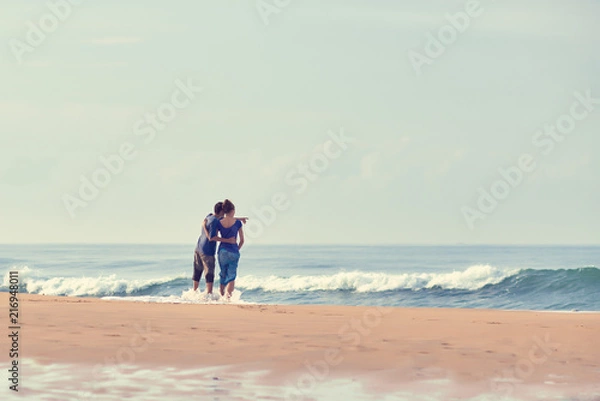 Fototapeta Young Couple standing on beach and looking to a sea. A man is showing his hand in the sea.