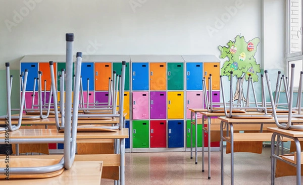 Fototapeta Empty Classroom with colorful lockers and raised chairs on the tables