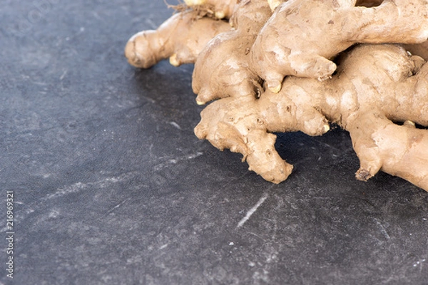 Fototapeta Whole ginger roots on dark old stone background table, space for text.