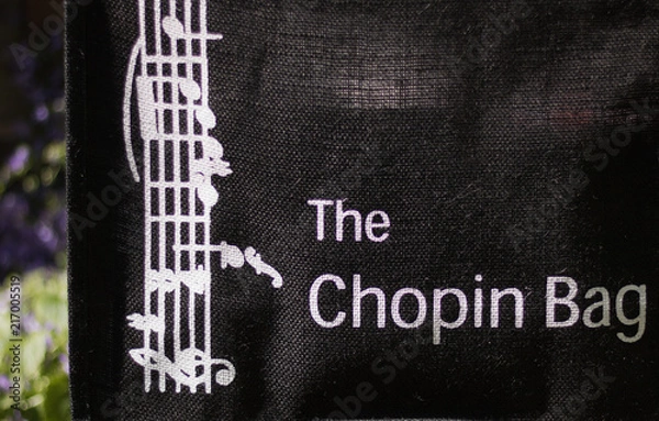 Fototapeta Chopin bag - these words with a sense of humor and music are on a natural sackcloth shopping bag. Green nature on a sunny day are on blurred background. Play of words. Shopping with pleasure.
