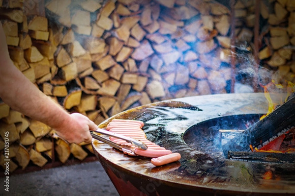 Obraz man frying sausages on a round grill