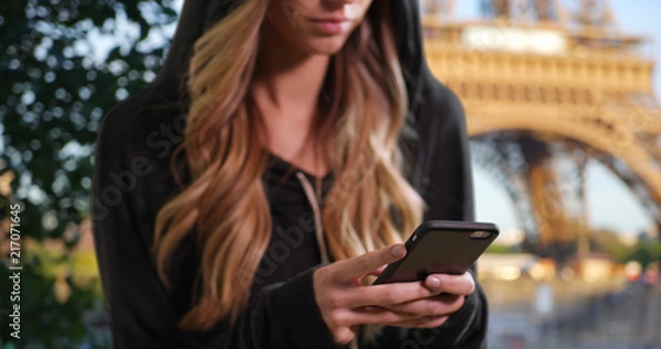 Fototapeta Blonde female in a hoodie texting with mobile phone in Paris