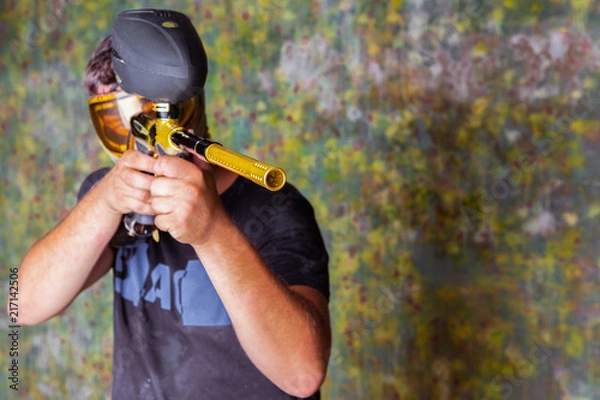 Fototapeta Paintball player in t-shirt shooting target with gun on