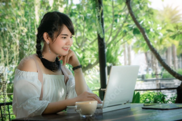 Fototapeta asian girl's sitting and using laptop looking smile on work in the cafe