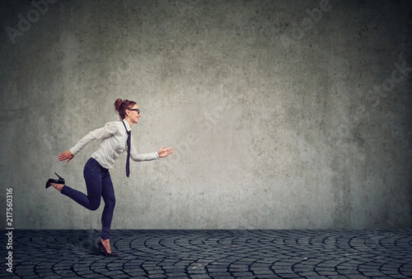 Fototapeta Businesswoman running against gray wall