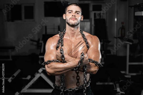 Fototapeta Muscular man slave in chains in gym, the prisoner