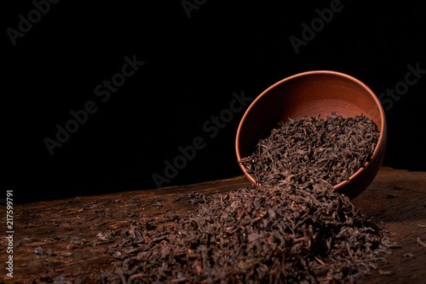 Obraz Dry tea leaves in clay bowl on black background. selective focus