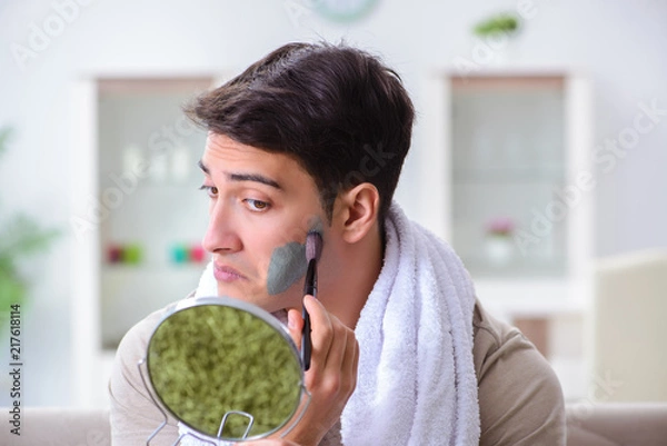 Fototapeta Handsome applying clay mask on face